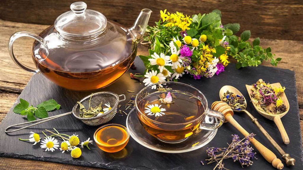 قوری شیشه‌ای در حال دم کشیدن دمنوش گیاهی رنگارنگ