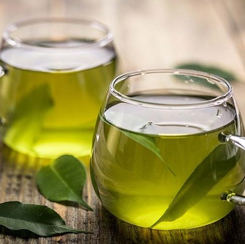 فنجان چای سبز با برگ‌های چای در کنار آن